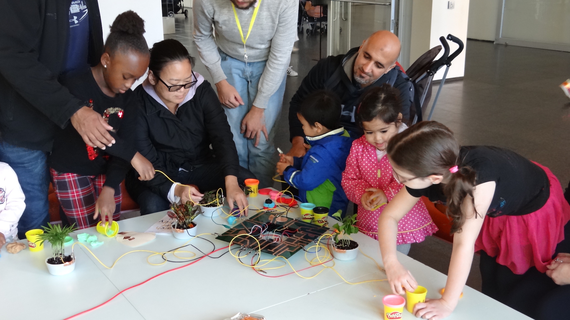a family gathered by a table, playing with conductive circuits